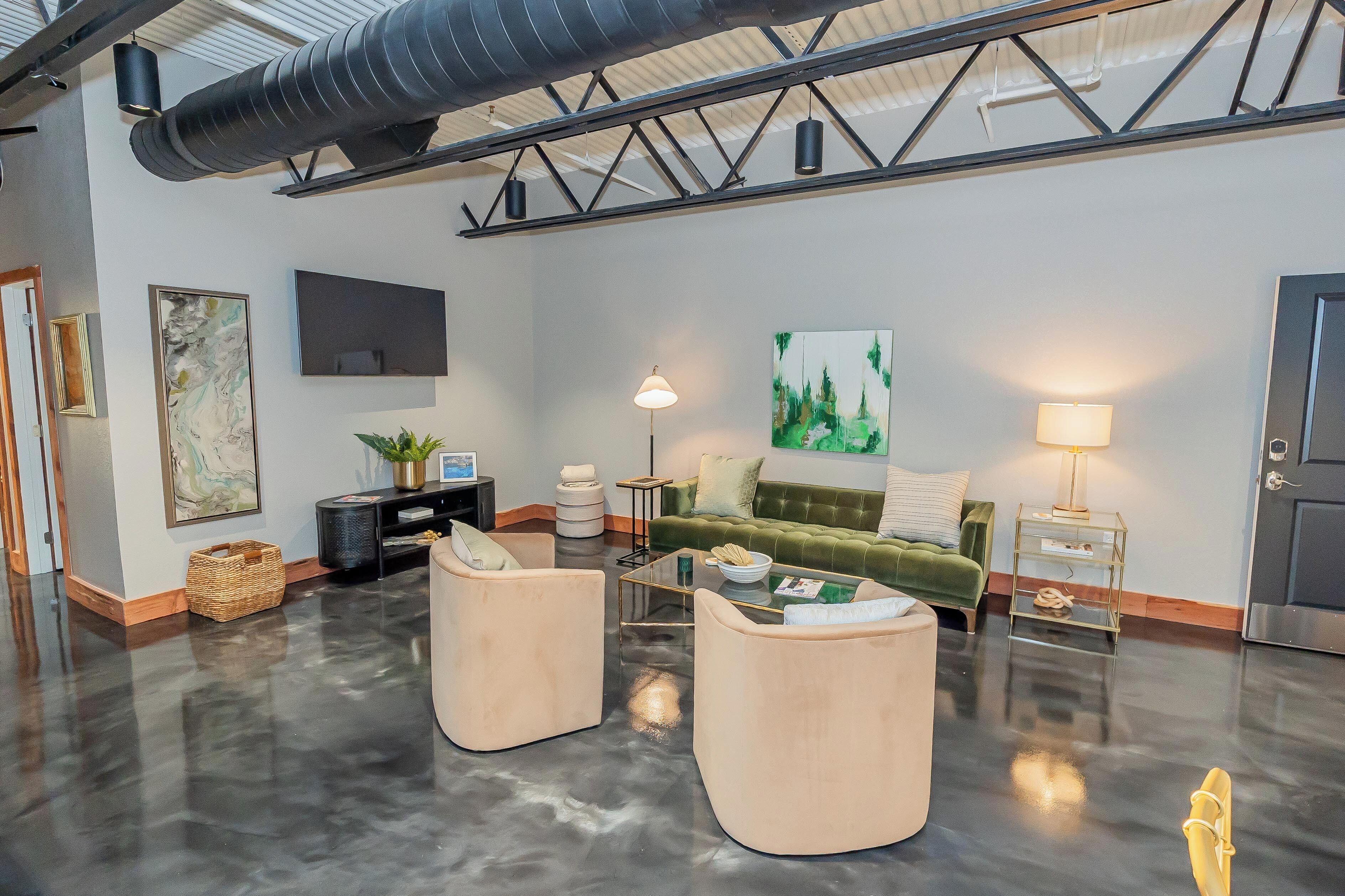 A spacious living area with a green sofa, two armchairs, a flat-screen TV, and a painting on the wall.