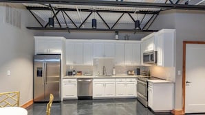 A modern kitchen with white cabinets, stainless steel appliances, and a polished concrete floor.