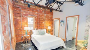 Ein Schlafzimmer mit Backsteinwand, einem Bett mit weißer Bettwäsche, zwei Nachttischlampen und einem kleinen Tisch mit einer Lampe.