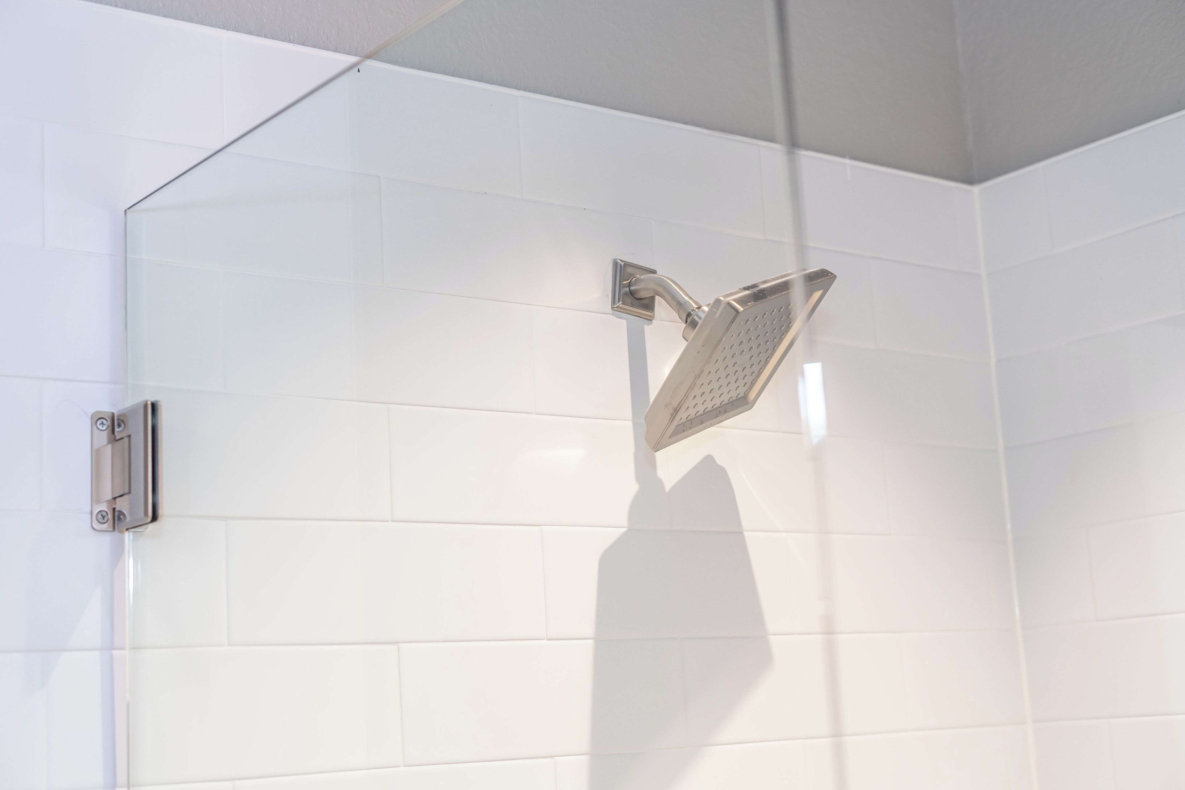 Une douche équipée d’un pommeau de douche à main fixé sur un mur recouvert de carreaux blancs.