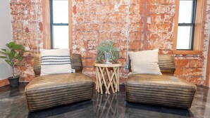 Ein Zimmer mit zwei Ledersofas, einem kleinen Holztisch mit Pflanze und einer Ziegelwand mit großen Fenstern.