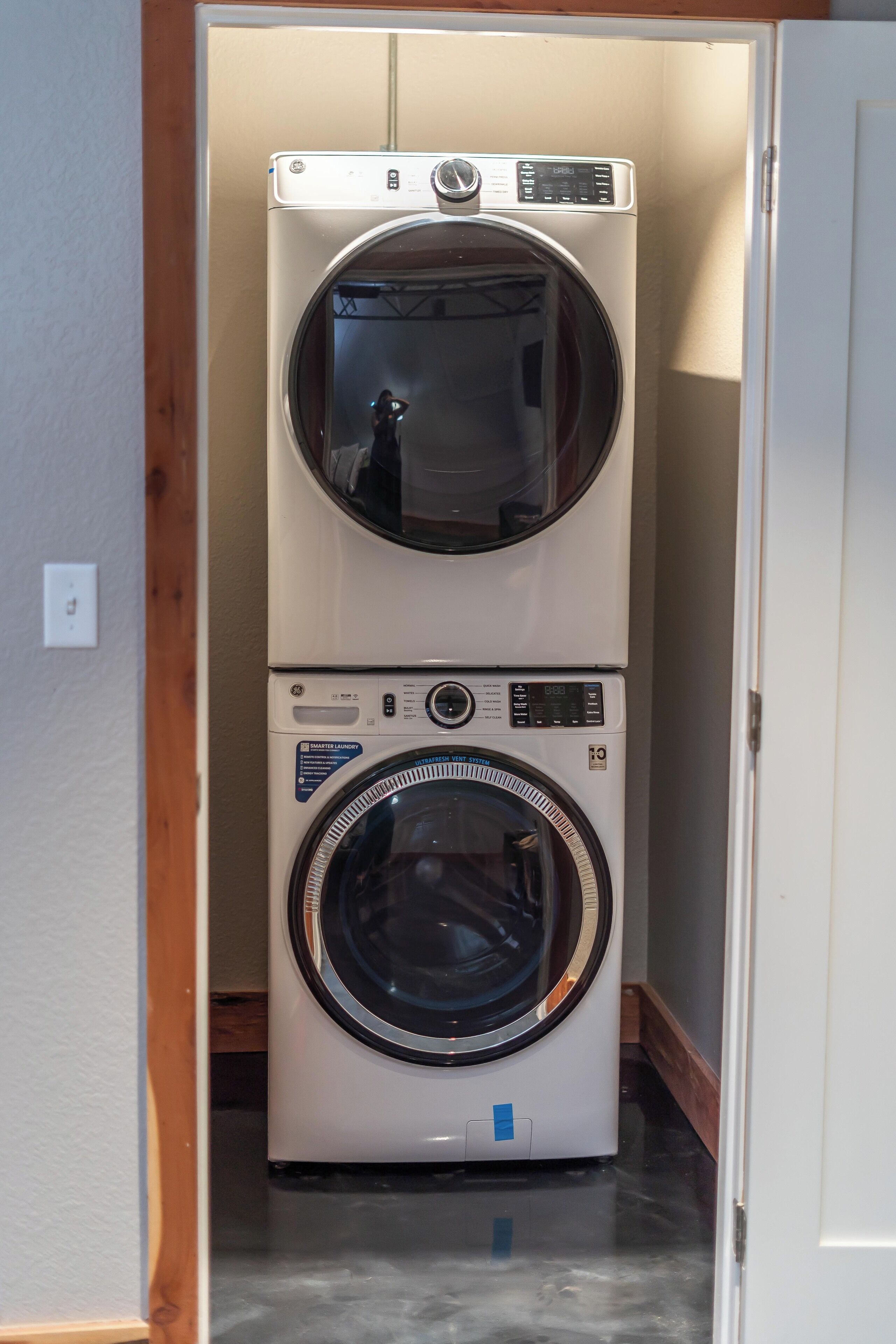 A stacked washer and dryer unit in a laundry room with a wooden floor and white walls.