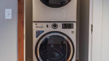 A stacked washer and dryer unit in a laundry room with a wooden floor and white walls.