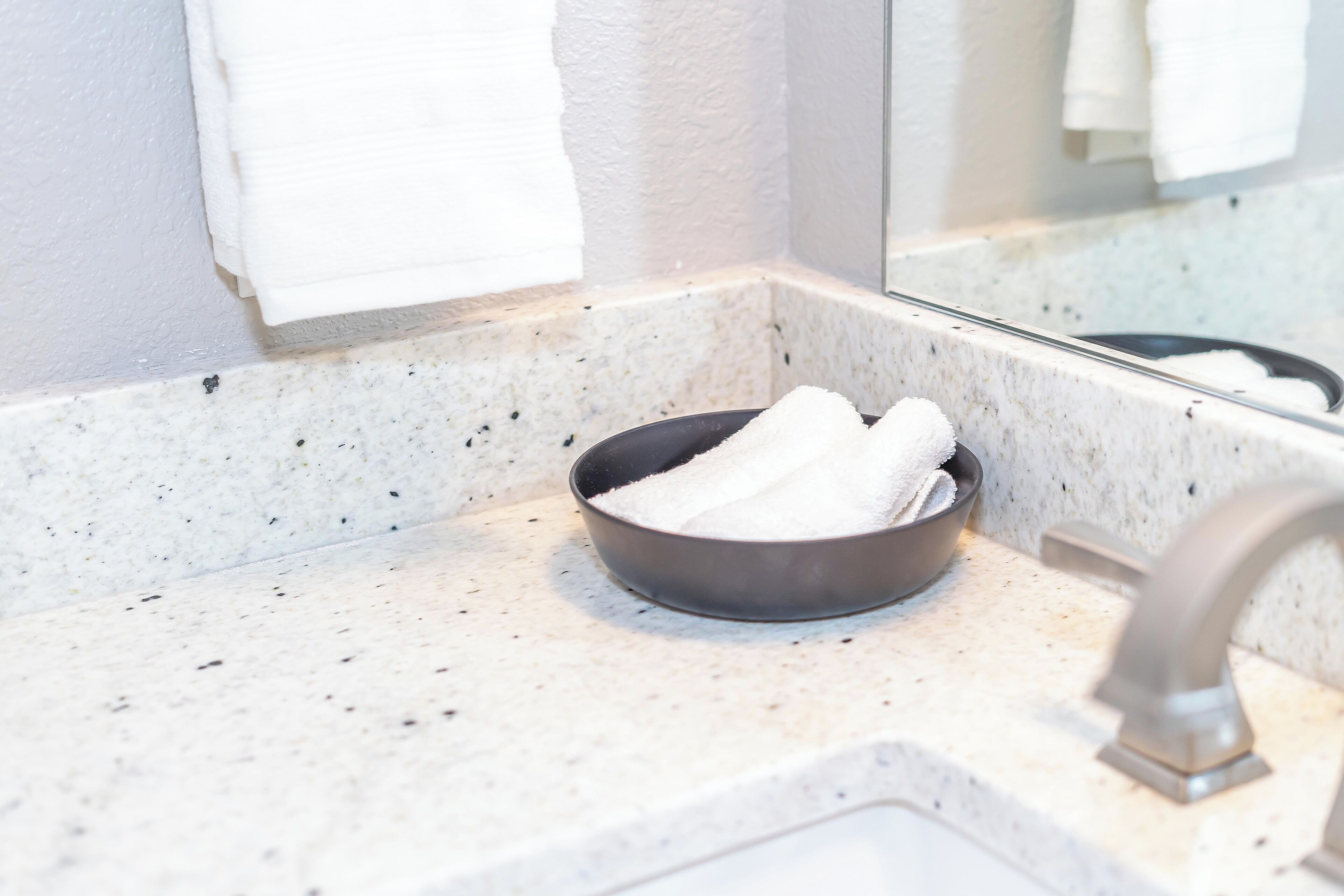 A bathroom sink with a bowl containing a white towel, a mirror reflecting a towel, and a faucet.