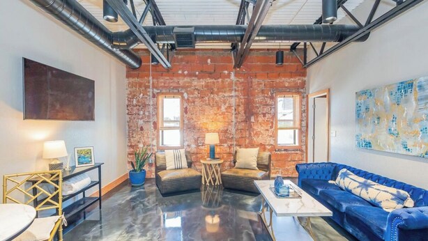 Ein geräumiges Wohnzimmer mit poliertem Betonboden, einem blauen Sofa, einem Couchtisch und einer Ziegelwand.