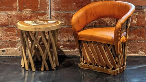A rustic room with exposed brick walls, a polished concrete floor, a wooden chair, and a small wooden table with a magazine.