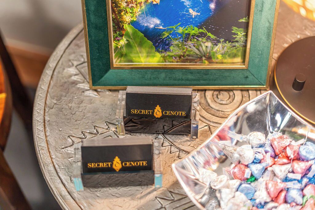 A table with a framed picture, two boxes labeled 'SECRET CENOTE', and a bowl of colorful candies.