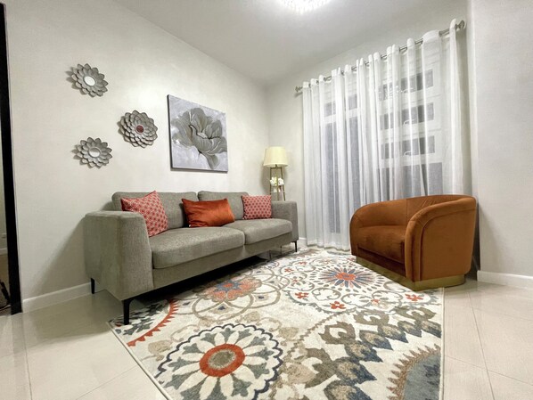 Una sala de estar con un sofá gris, un tapete estampado, decoración en la pared y un sillón marrón.