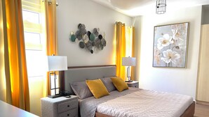A modern bedroom with a large bed, two bedside tables, a nightstand, and a wall-mounted lamp.
