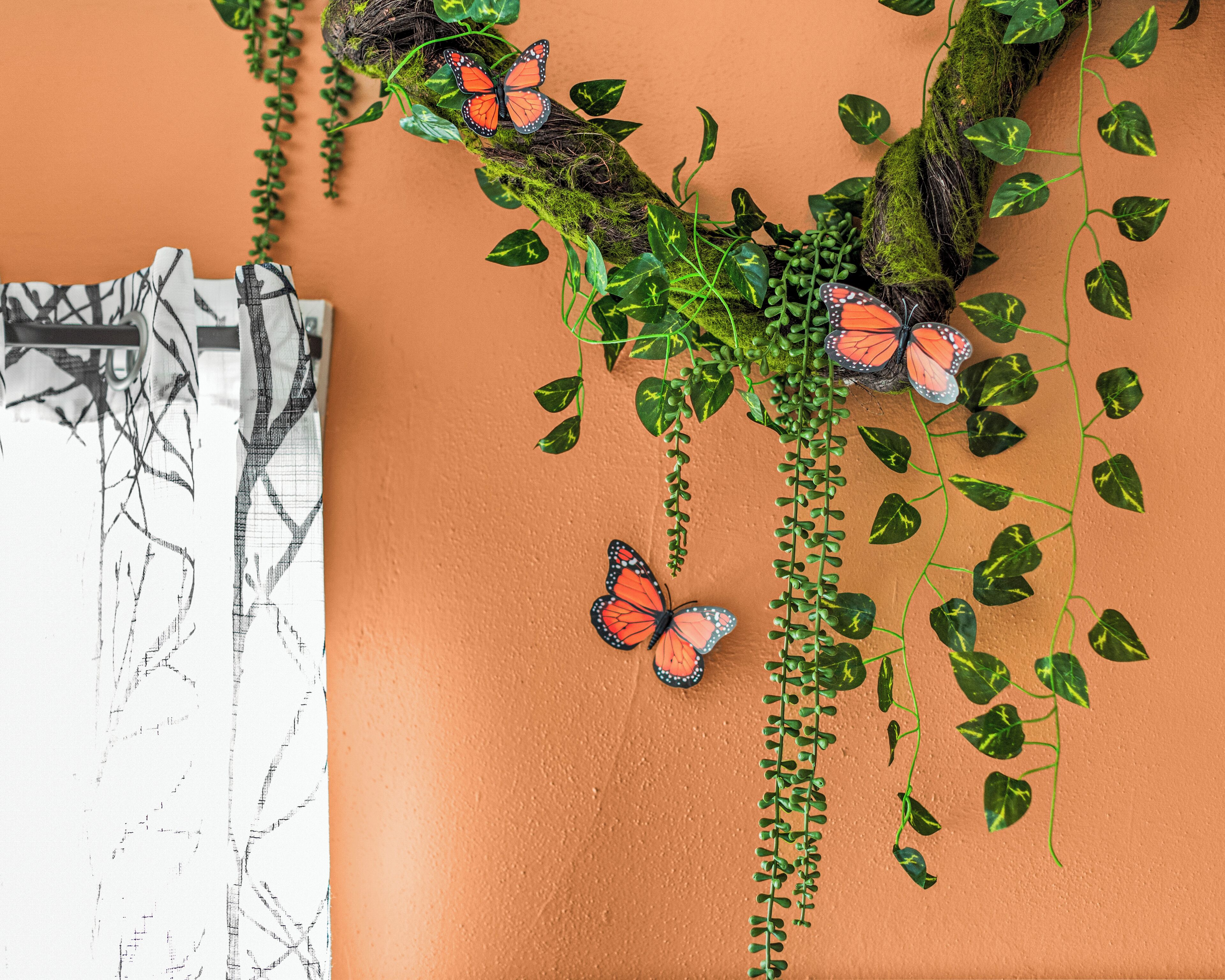 A wall with a textured surface, green vines, and orange butterfly decorations.