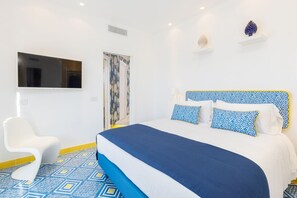 Un dormitorio moderno con una cama grande, una silla blanca y un televisor montado en la pared.