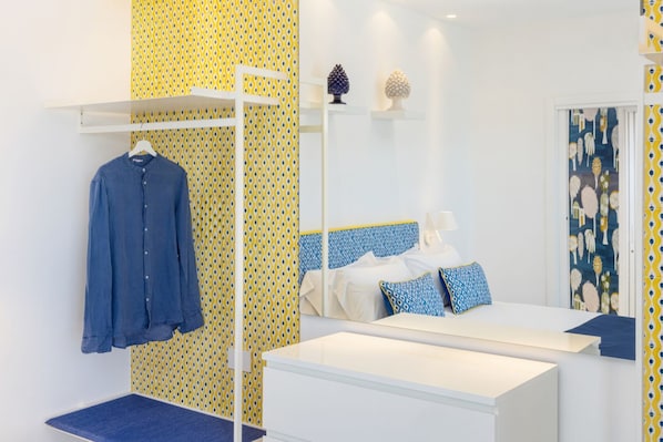 A bedroom with a bed, a bedside table, a hanging rack with clothes, and patterned wallpaper. - Stylish & Elegant Flat with Terrace (Sorrento)