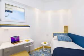 Een kamer met een bed, een bureau met een laptop, een klein tafeltje en een raam.