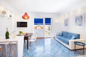 A modern living room with a blue patterned floor, a white sofa, a dining table with chairs, and a TV mounted on the wall. - Stylish & Elegant Flat with Terrace (Sorrento)