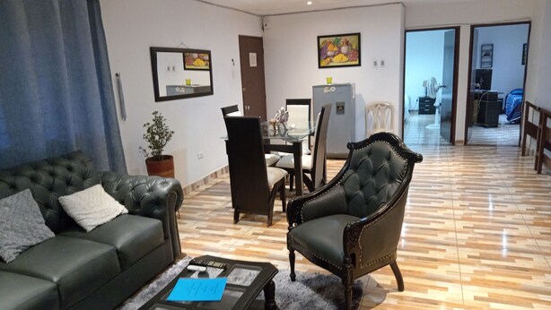 A living room with a sofa, armchair, coffee table, and dining area with chairs and a table.