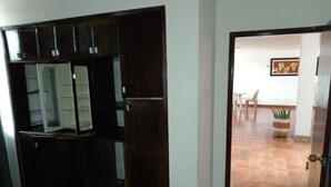 A room with a bed, a wardrobe, and a door leading to a dining area with a table and chairs.