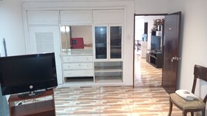 A room with a television on a wooden stand, a wardrobe with mirrored doors, a bench, and a door leading to another room.
