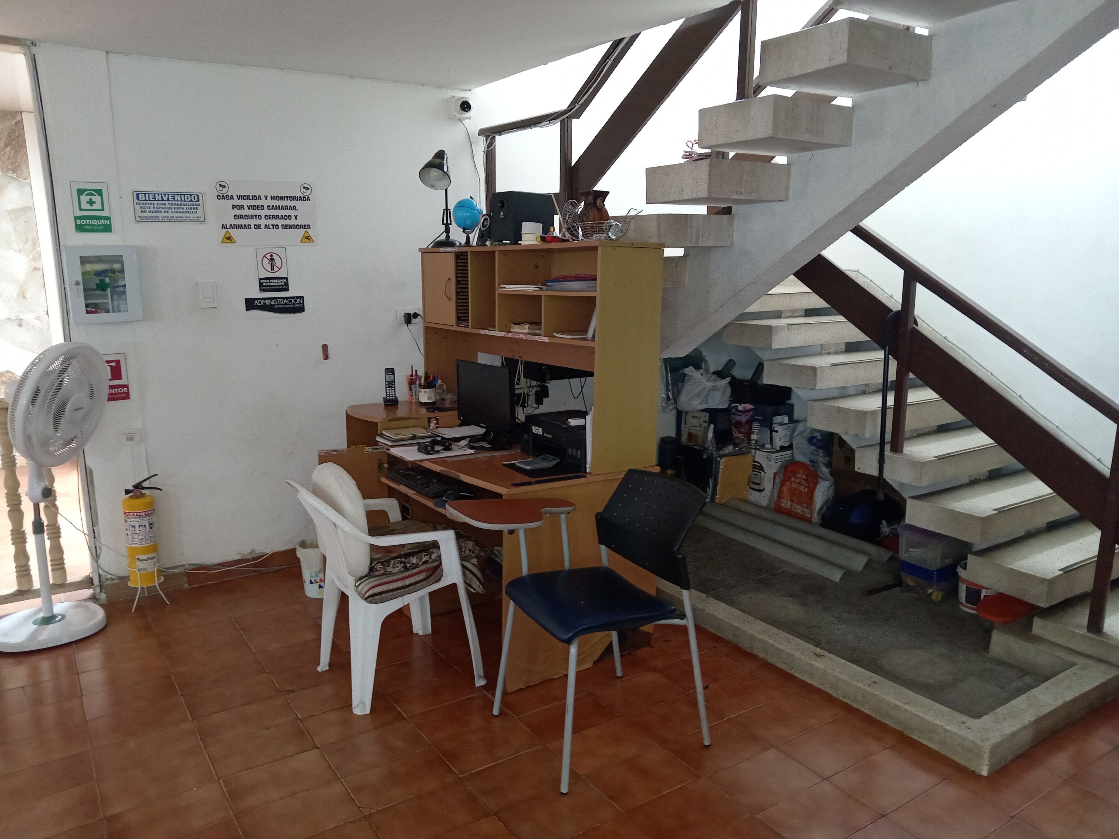Een kantoorruimte met een bureau, computer en stoelen. Er is een trap met een metalen leuning.