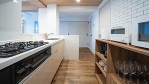 Een moderne keuken met een gasfornuis, oven, magnetron en houten planken met wijnglazen.