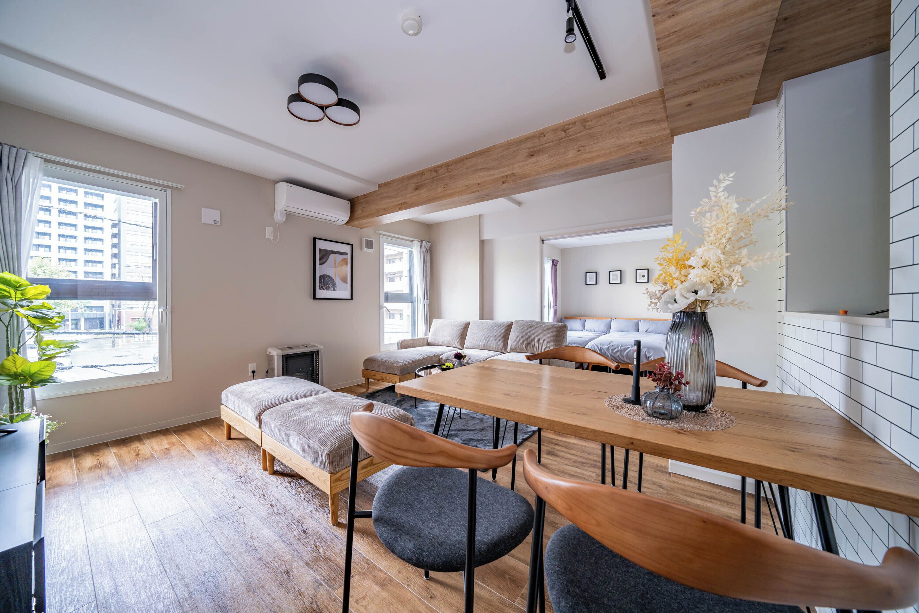 A modern living room with a wooden dining table, grey upholstered chairs, and a sofa set.