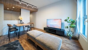 Een moderne woonkamer met houten vloer, een bank, een eettafel met stoelen, een televisie en een potplant.