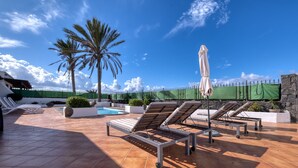 A rooftop pool area with lounge chairs and umbrellas, surrounded by a green fence and palm trees. - Villa Arena Blanca - Pool, Ping-pong and BBQ By LVH (Playa Blanca)