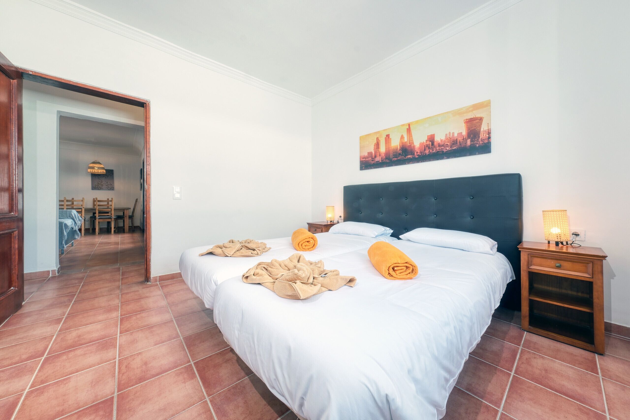 Une chambre d’hôtel avec un grand lit, une table de chevet avec une lampe et un tableau représentant un paysage urbain accroché au mur.