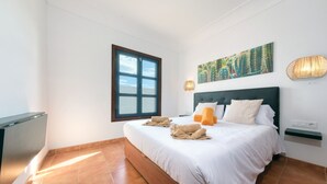 A bedroom with a large bed, a window, a wall-mounted artwork, and a bedside lamp. - Villa Arena Blanca - Pool, Ping-pong and BBQ By LVH (Playa Blanca)