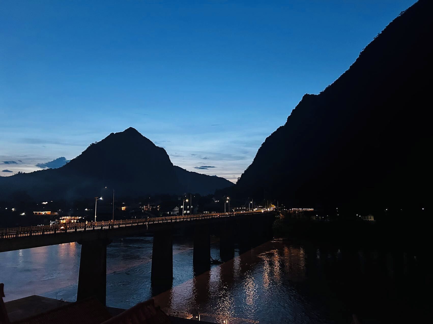Vista nocturna de un puente sobre un río con montañas al fondo.