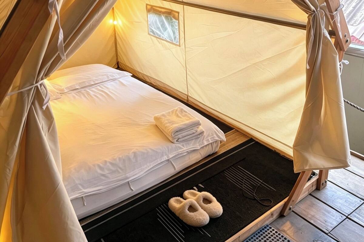 Ein Zelt mit einem Bett, einem kleinen Fenster und einem Paar Hausschuhen auf dem Boden.