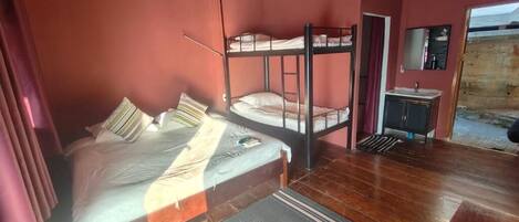 A room with a bunk bed, a bedside table with a mirror, and a small cabinet.
