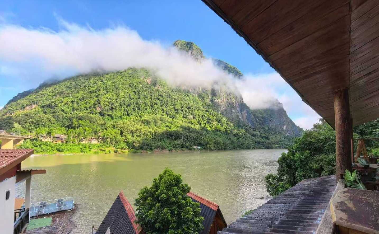 A view of a river with a mountain in the background, a wooden staircase, and a building with a red roof.