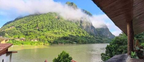A view of a river with a mountain in the background, a wooden staircase, and a building with a red roof.