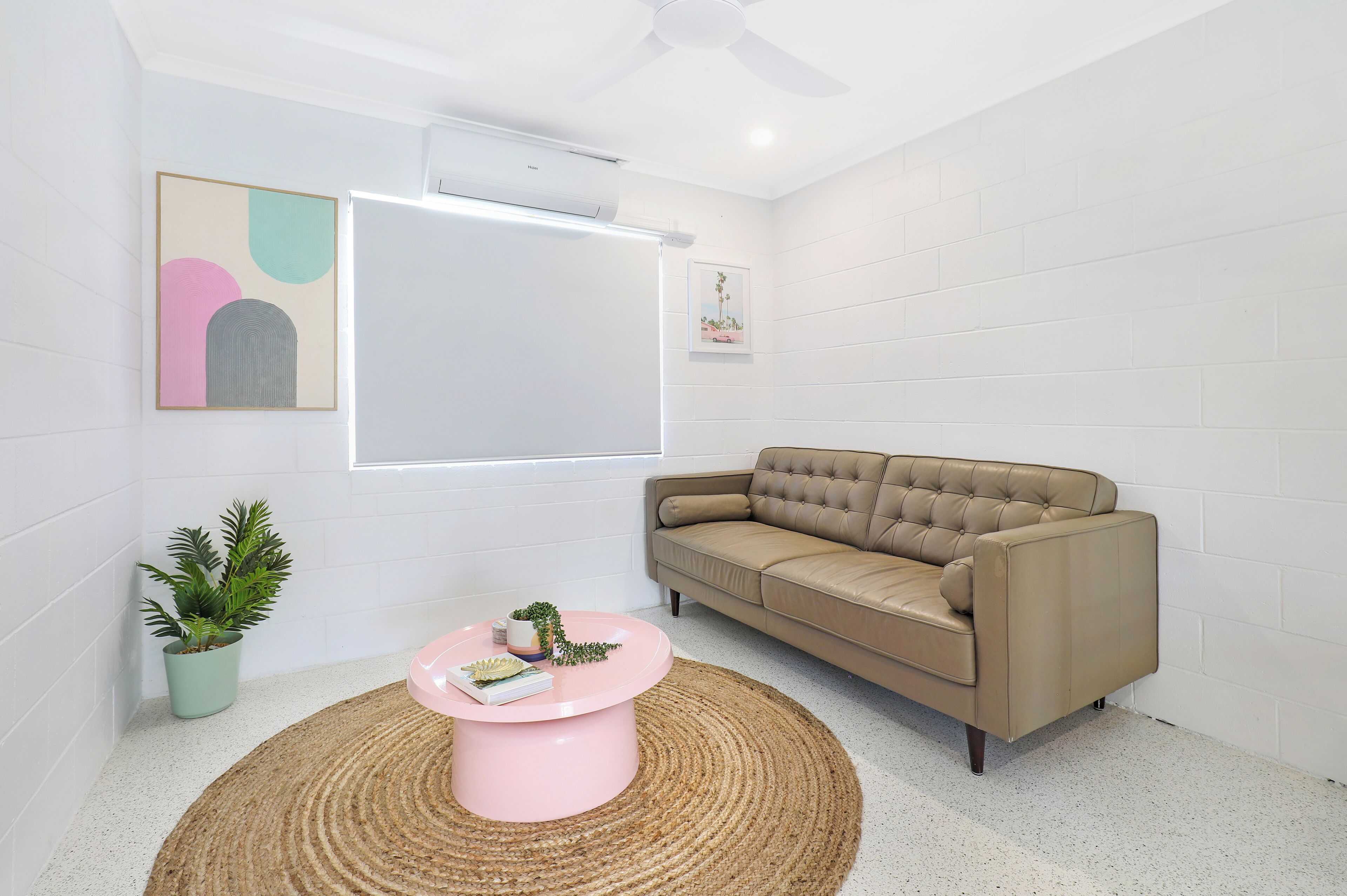 A modern living room with a beige sofa, a pink coffee table, a potted plant, and a framed artwork on the wall.