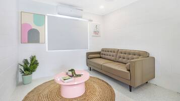 A modern living room with a beige sofa, a pink coffee table, a potted plant, and a framed artwork on the wall.