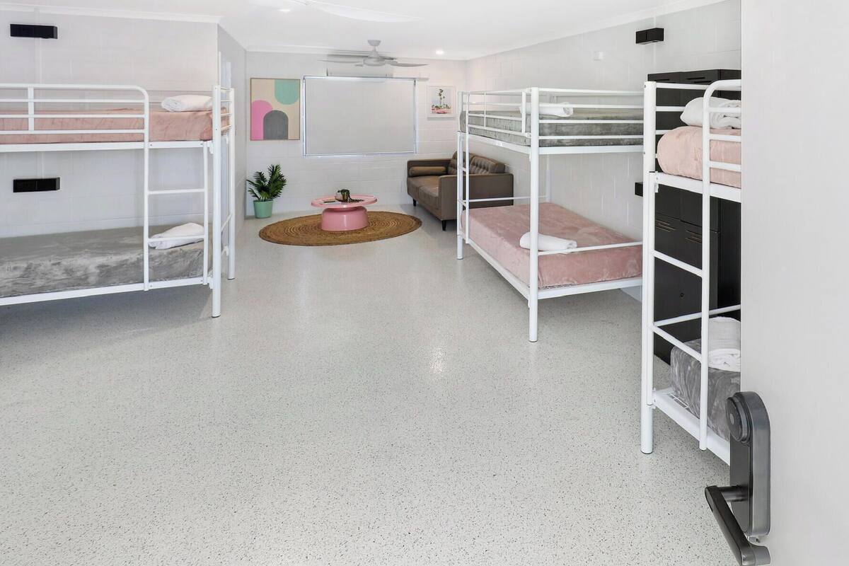 Una habitación con literas, una mesita redonda con un bol rosa, un sofá y una planta en maceta.