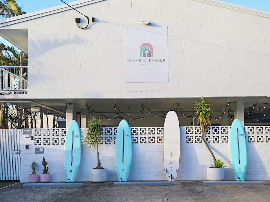 Un edificio con un cartel que dice 'Palms on Parker Hostel' y varios botes de surf montados en la pared.