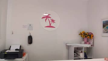 Zona de recepción con mostrador, una impresora, un cartel en la pared con palmeras y una estantería con girasoles.