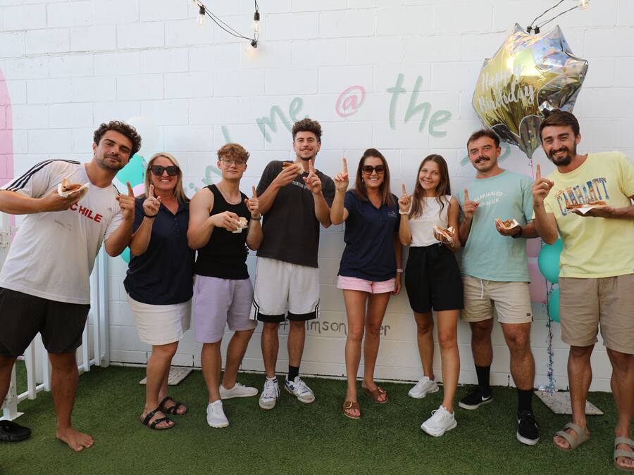 Un grupo de personas de pie en un interior con una pared blanca y un piso de césped artificial verde.