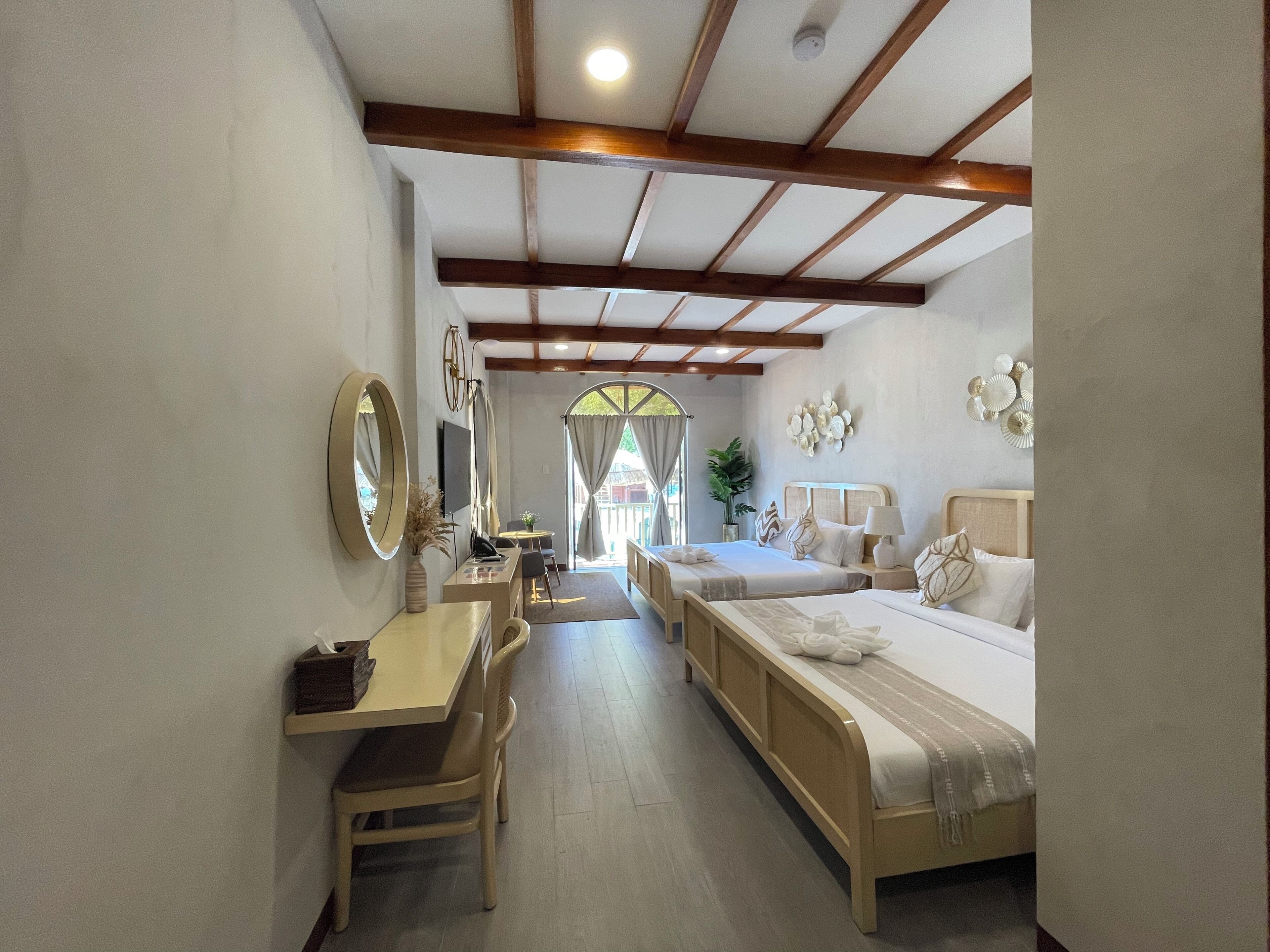 A hotel room with a desk, two beds, a TV, and a large mirror.
