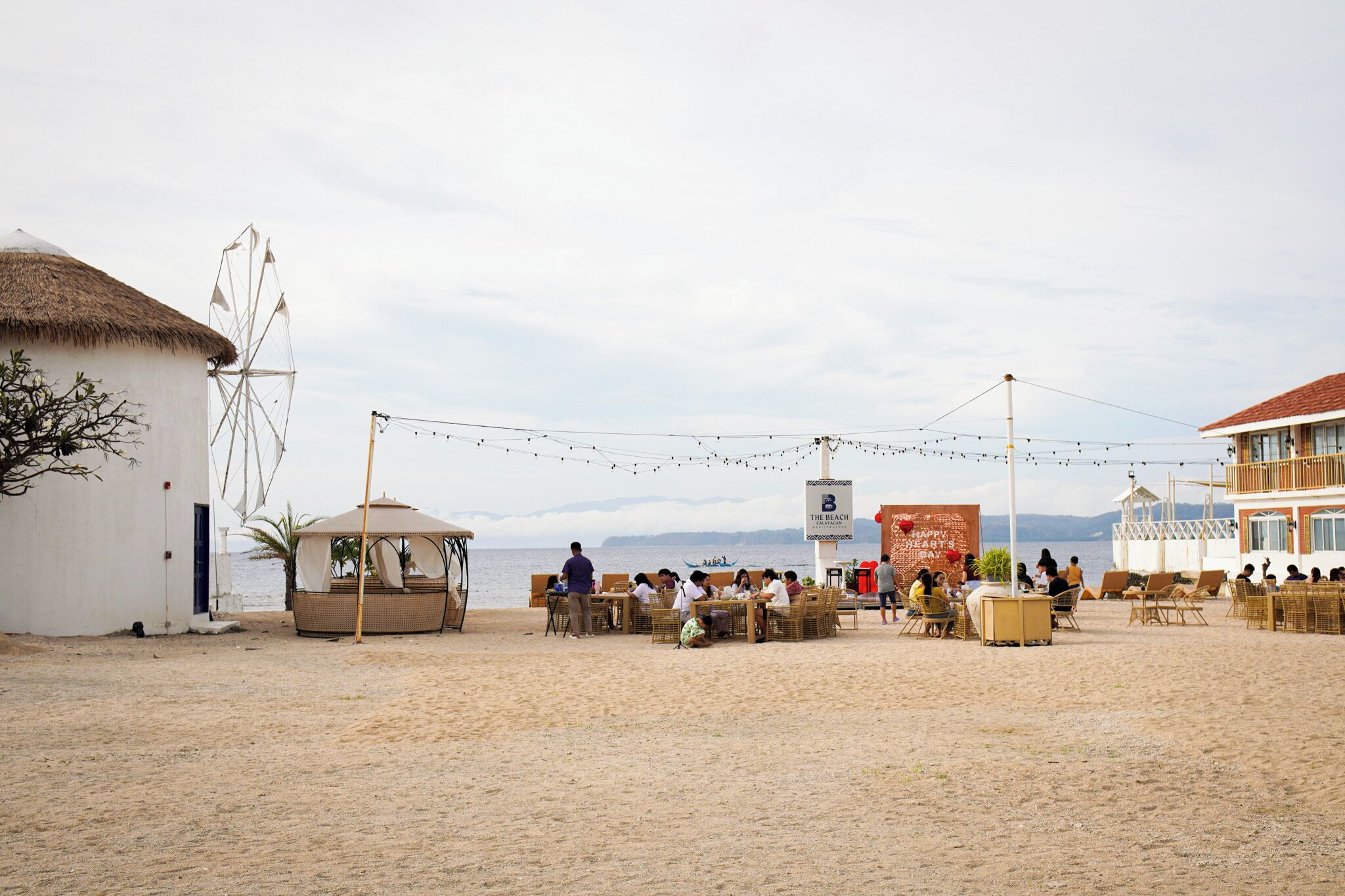 A beachside restaurant with outdoor seating, a thatched-roof building, and a sign indicating 'The Beach'.