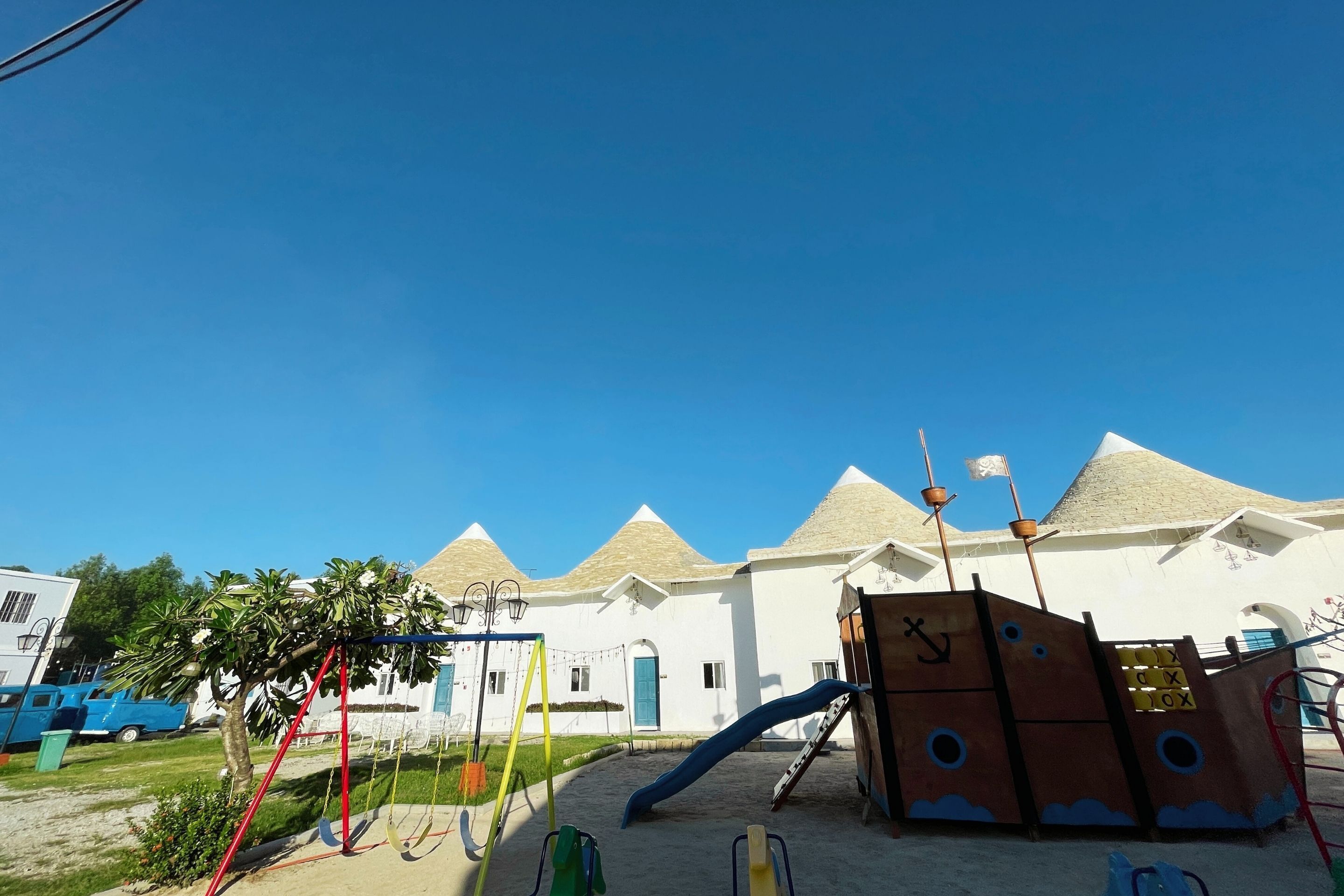 A playground with swings, slides, and climbing structures in front of a white building with conical roofs.