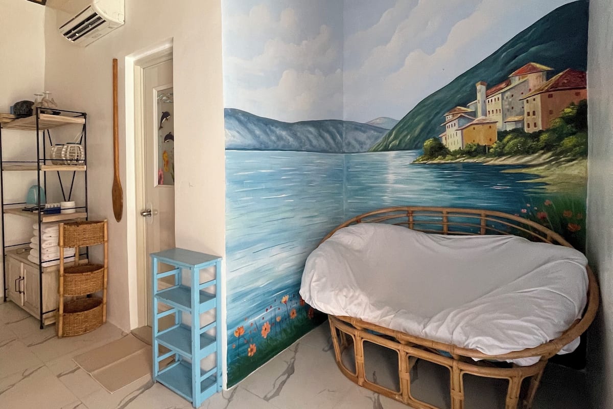 A bedroom with a mural of a lake, a bed, a shelf, and a wardrobe.