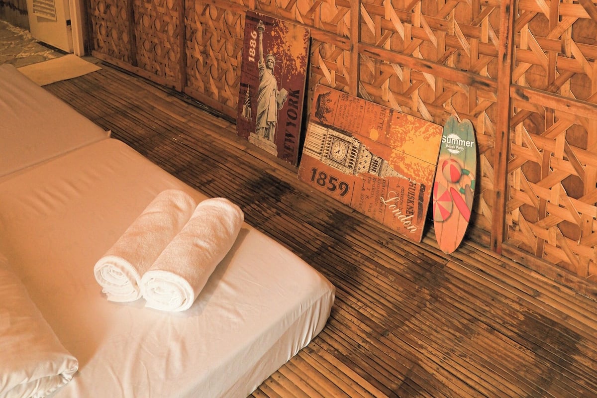 A neatly made bed with rolled towels, a wooden wall with historical plaques, and a wooden floor.