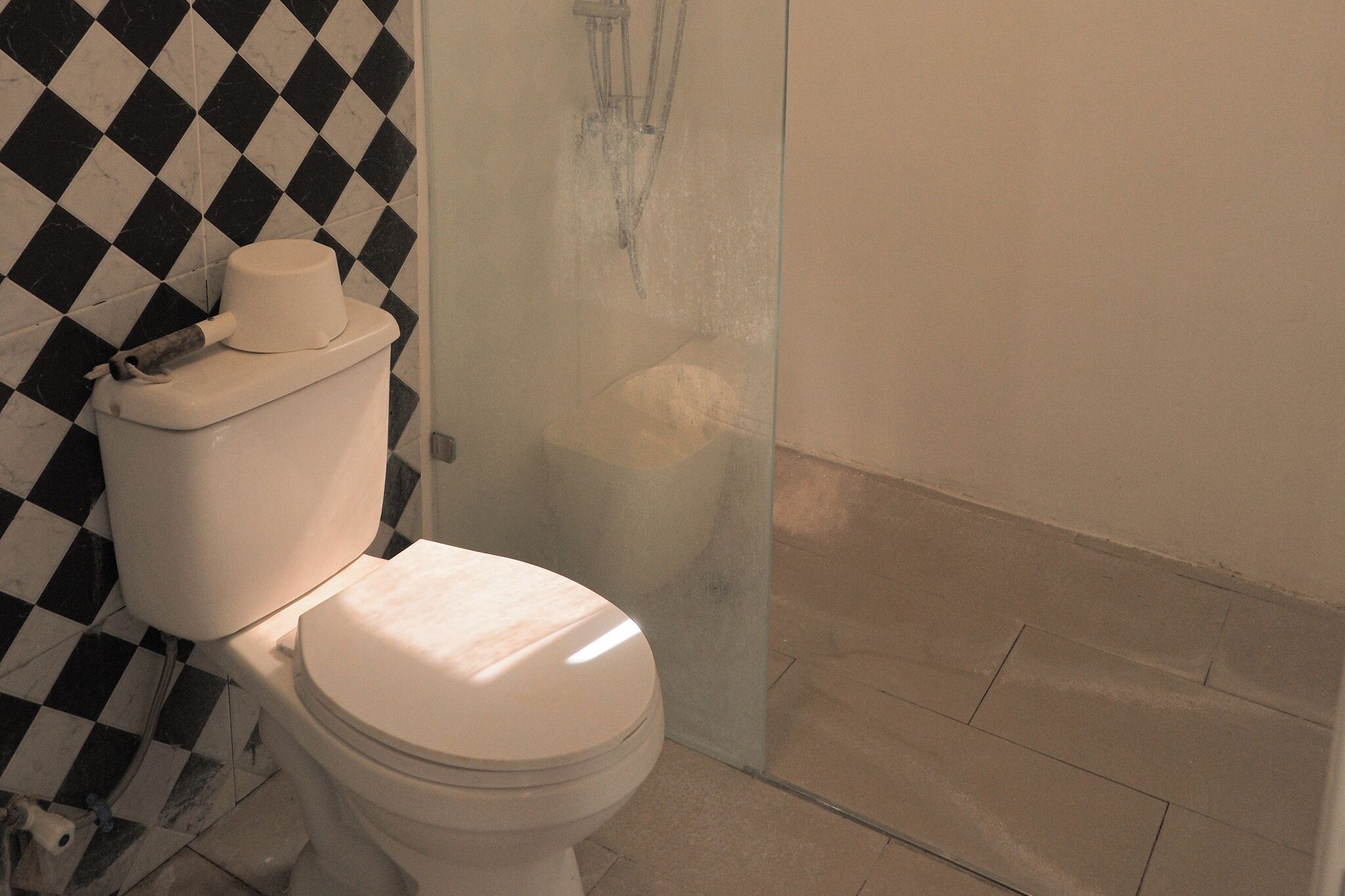 Un baño con inodoro, cabina de ducha de vidrio y suelo con estampado de cuadros.