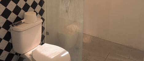 Un baño con inodoro, cabina de ducha de vidrio y suelo con estampado de cuadros.
