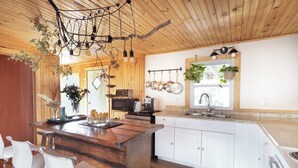 Eine Küche mit Holzausstattung, einer zentralen Kochinsel mit Barhocker, hängenden Töpfen und einer Pendelleuchte.