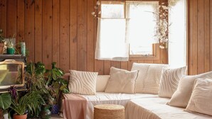 Ein gemütliches Zimmer mit Holzwänden, einem großen Fenster, einer Couch und einigen Blumentöpfen.
