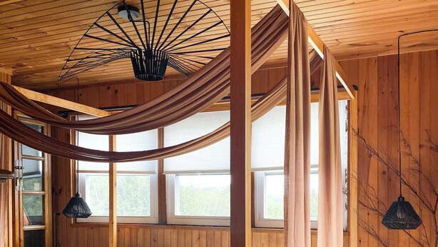 Ein Schlafzimmer einer Holzhütte mit einem großen Bett, einer Pendelleuchte und Blick ins Freie.