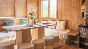 Ein gemütliches Blockhaus-Interieur mit Holzbalkendecke, einem zentralen Tisch, einer Bank und Korb-Hocker.